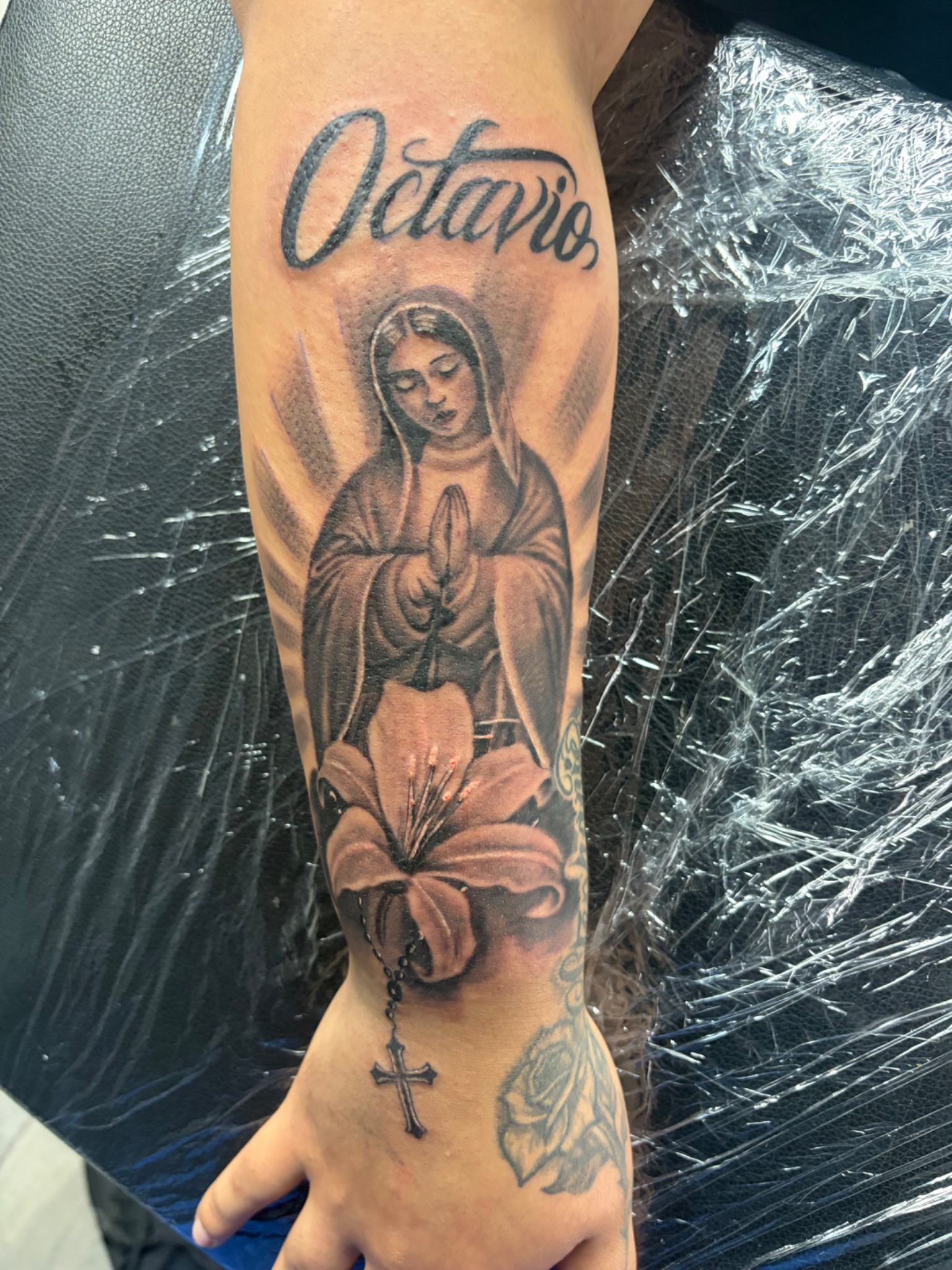 Black and grey Virgin Mary flowers and Octavio script tattoo